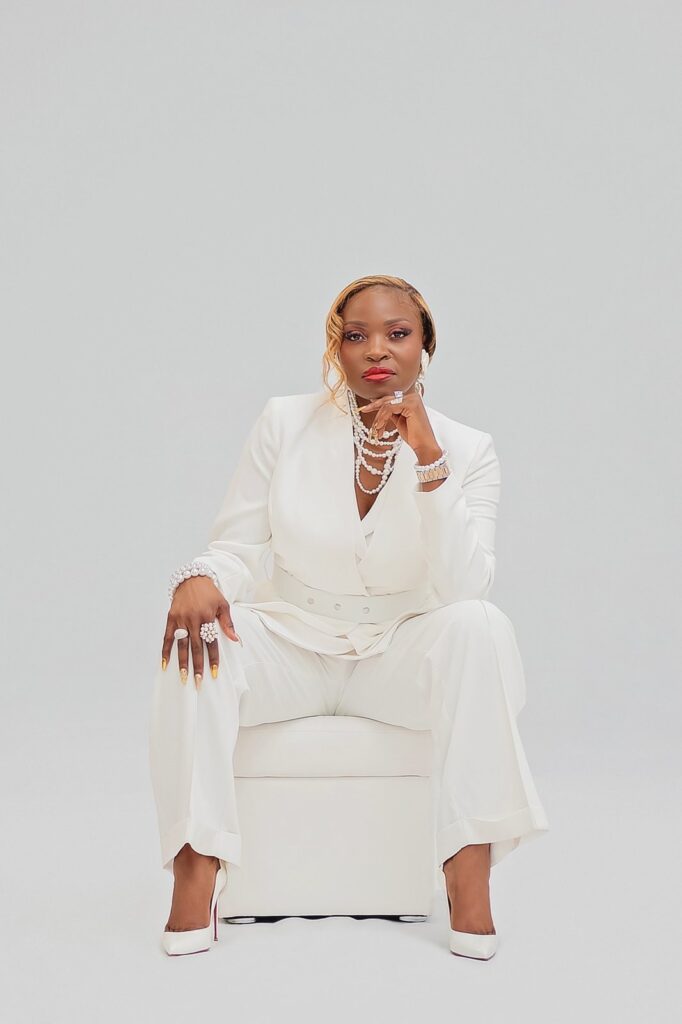 black American women sitting on a stool facing the camera. she is putting on a white female suit